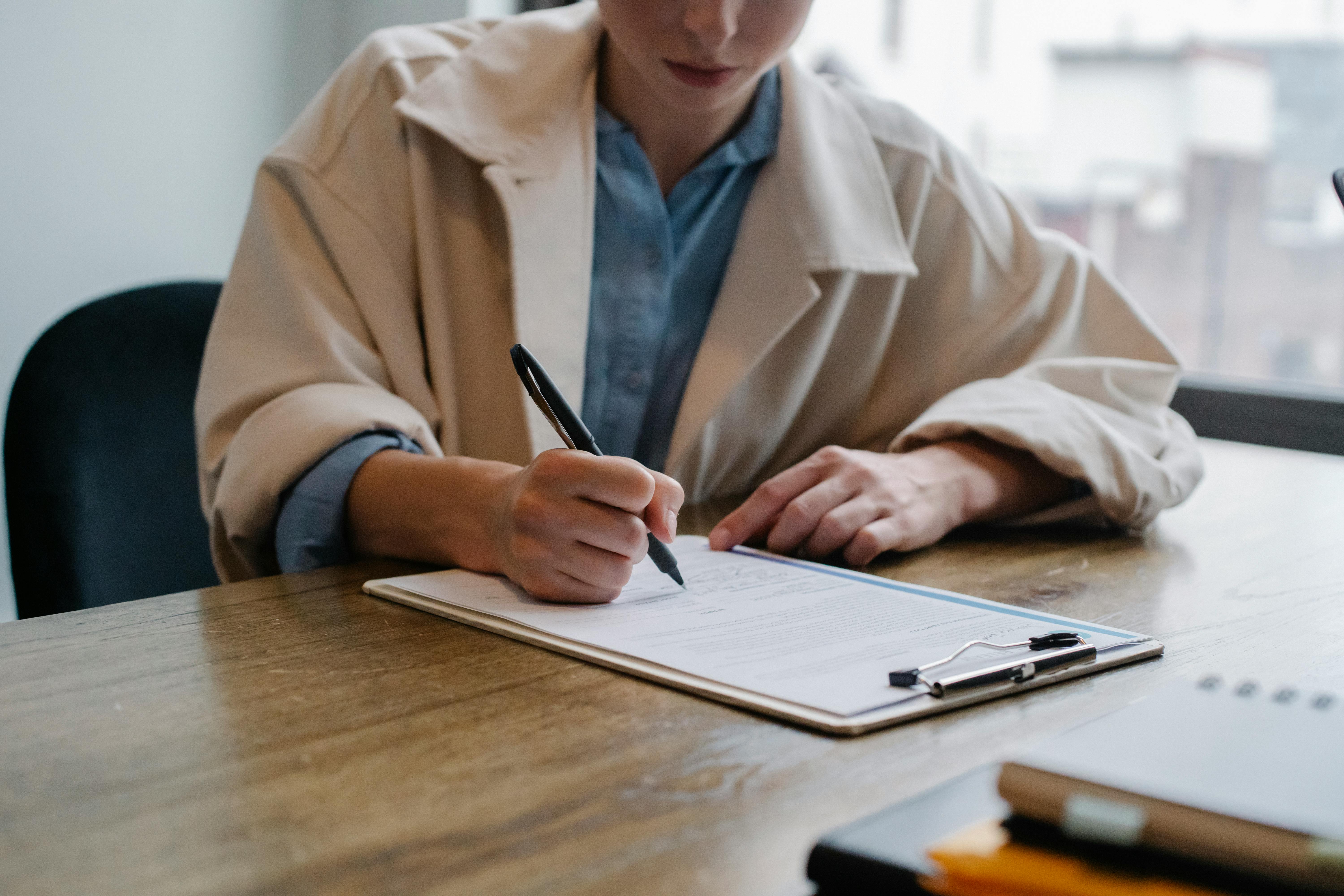 A person fills in a paper form on a clipboard with a pen.